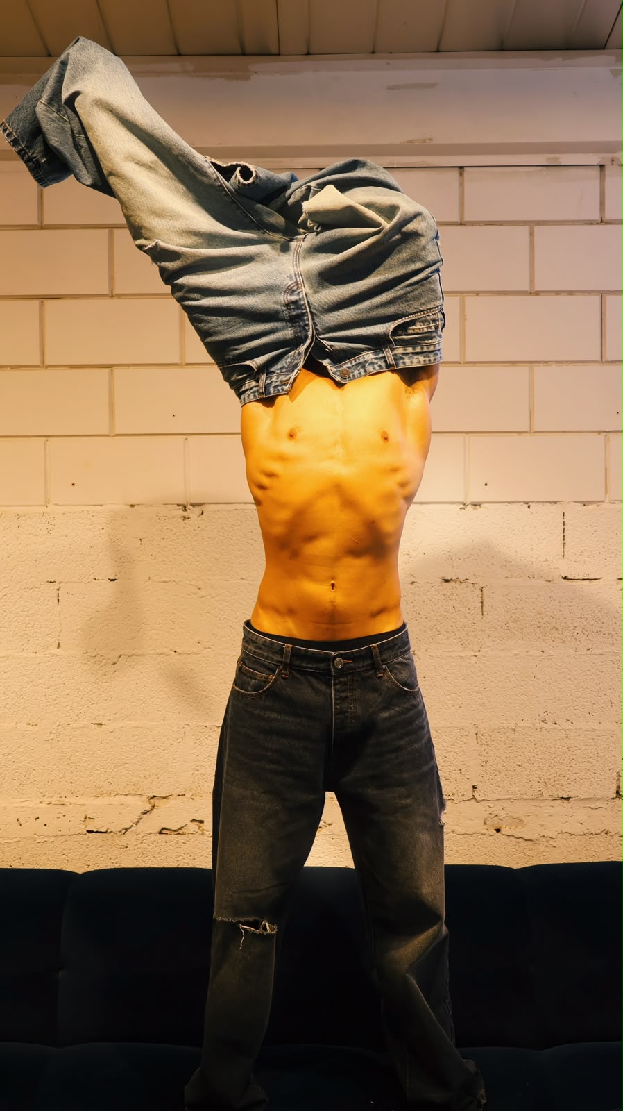 Male model standing against a white brick wall, wearing MFOURFIVE dark wash distressed denim jeans.