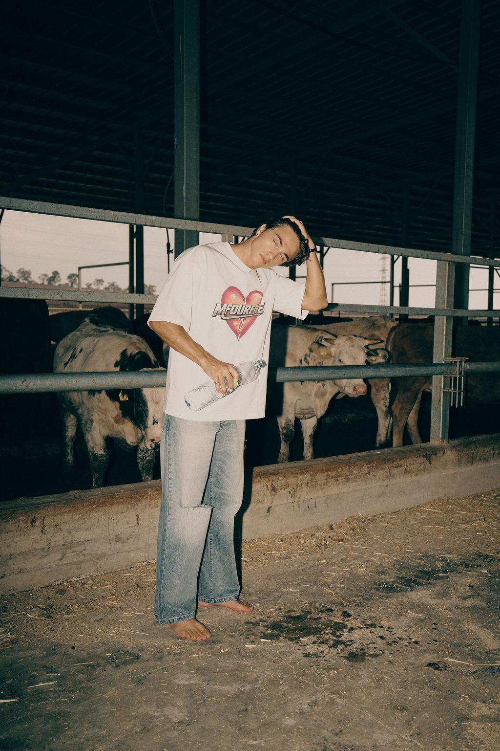Male model wearing white broken heart graphic t-shirt and ripped blue jeans in a barn