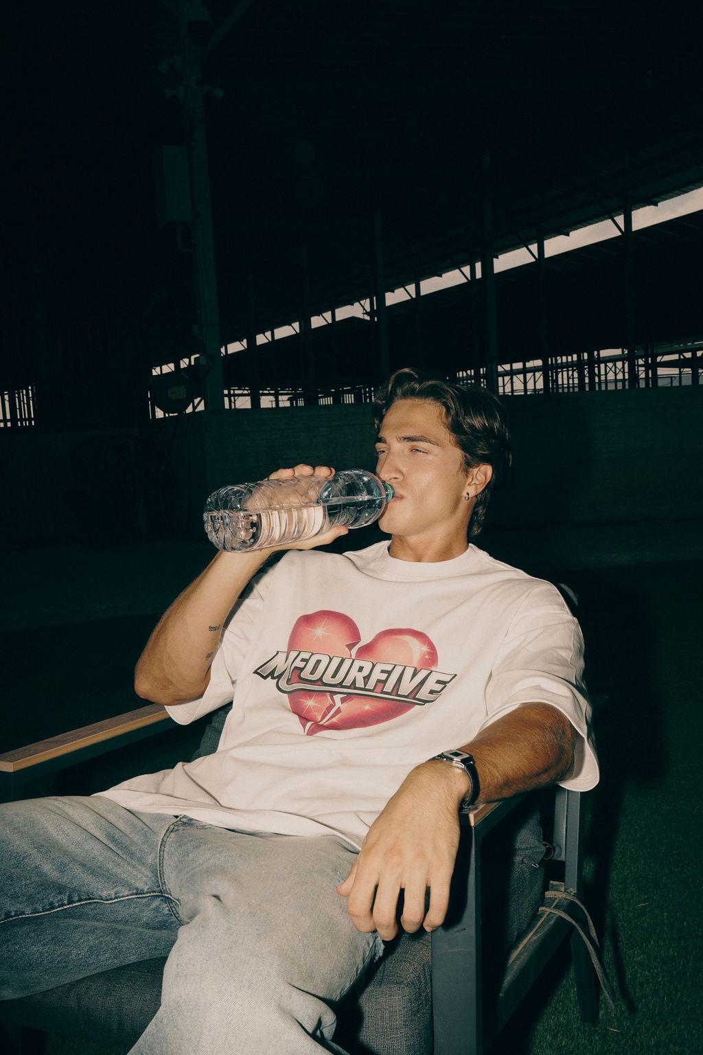 Male model seated wearing white broken heart graphic oversized t-shirt and jeans