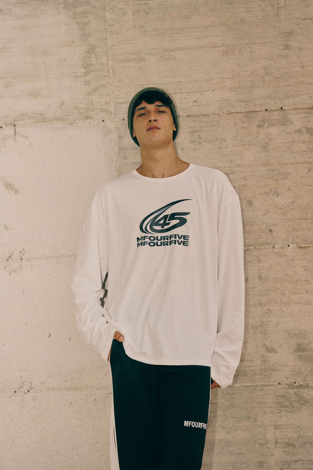 Male model wearing white long-sleeve graphic t-shirt, beanie, and track pants