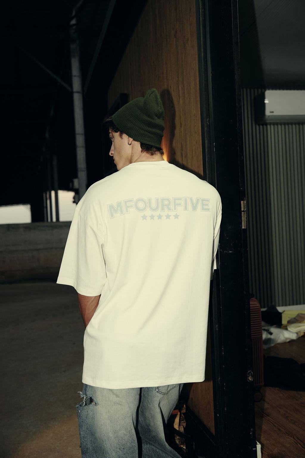 Back view of male model wearing white t-shirt with Mfourfive stars text logo and beanie